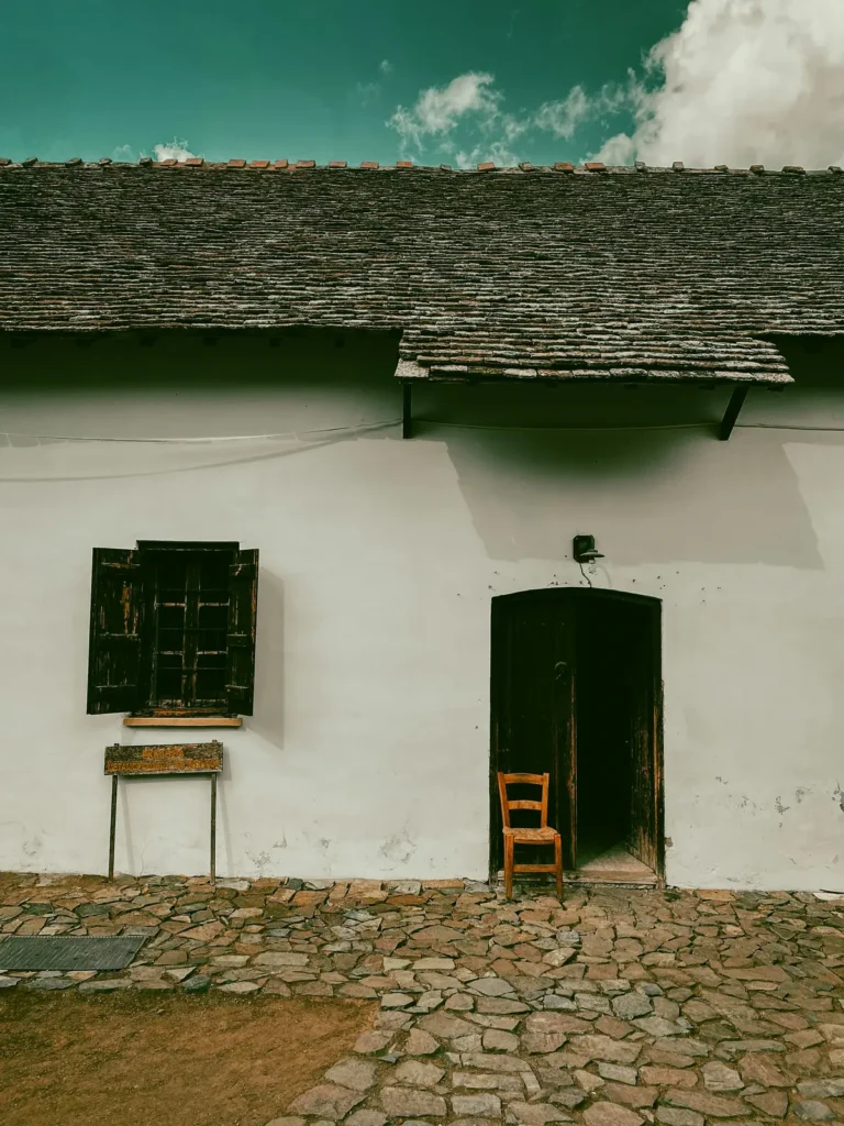 A weathered whitewashed wall with a wooden shutter, an old door and a single chair in a Troodos mountain village