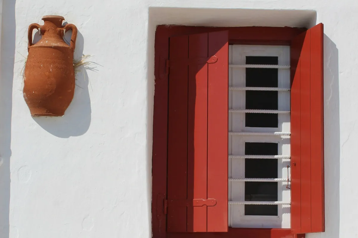 Greecyz A red wooden shutter and a clay amphora on a whitewashed wall in the Cyclades, Greece