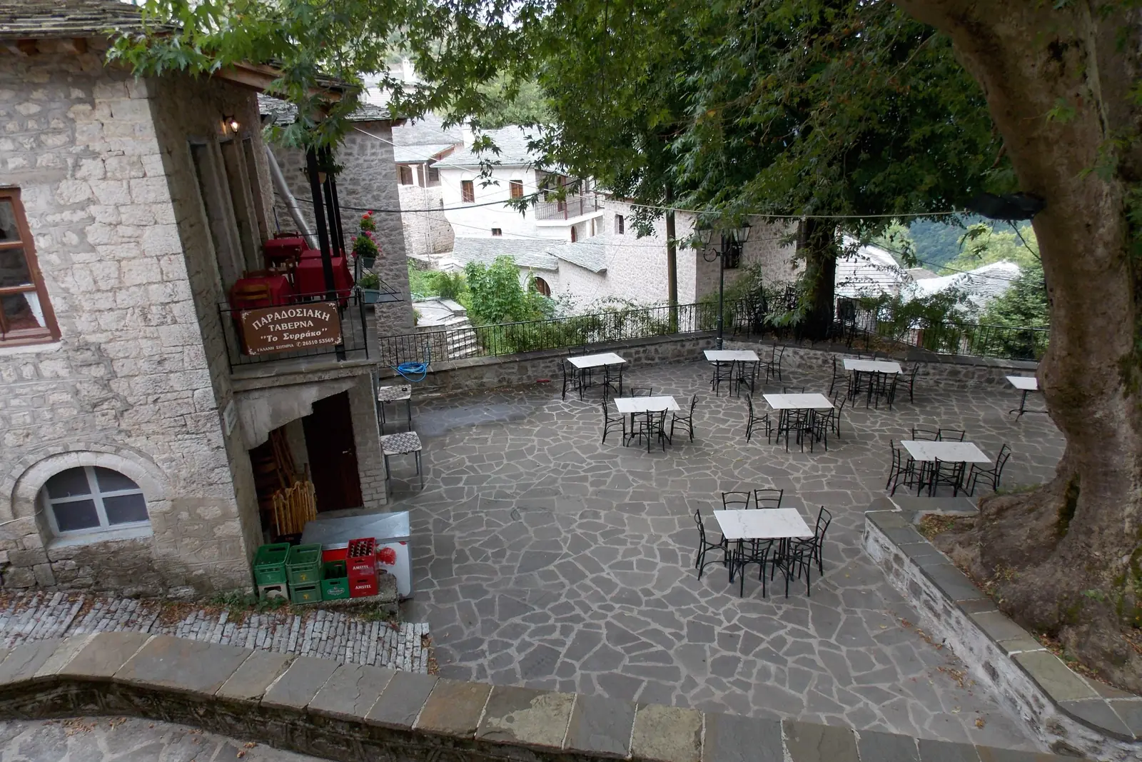 Stone-paved square in Syrrako with café tables in the shade of a large plane tree