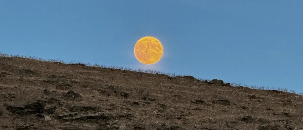 Large orange moon rising over the dry hillside above Skylou beach, Kythnos