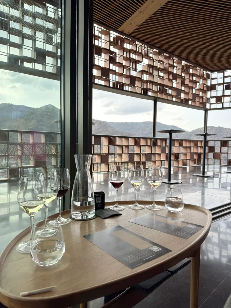 Wine tasting flight of white and red wines on a wooden table, with the winery terrace and Troodos mountains behind